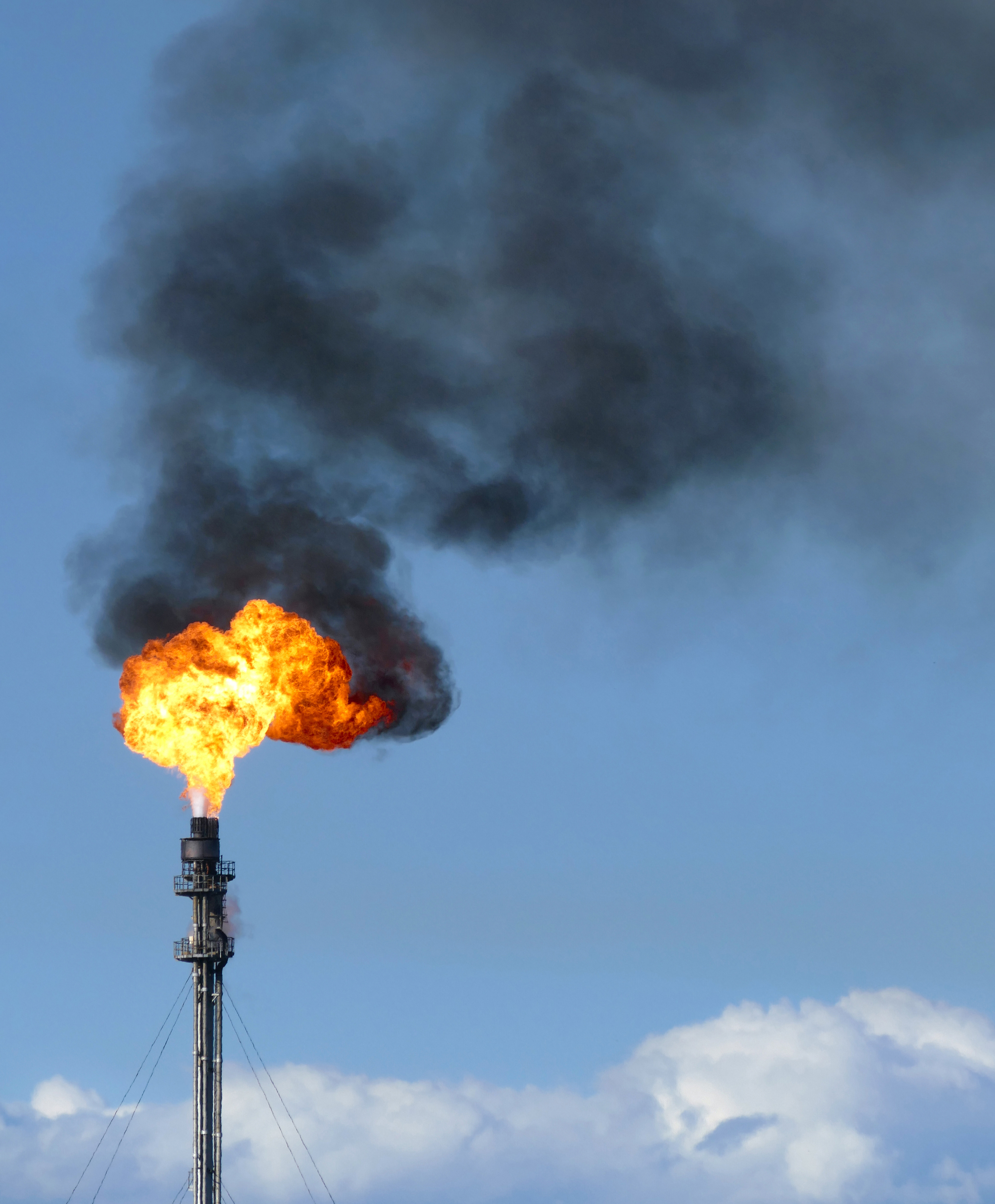 Gas flare fire and black smoke on blue sky day.