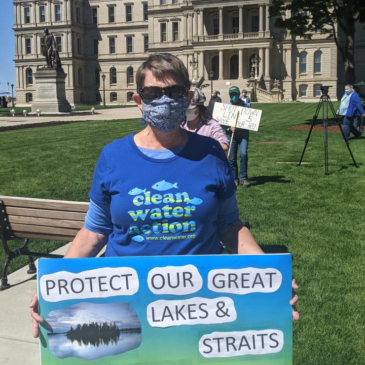 Protestor holding sign saying: "Protect Our Great Lakes & Straits, Shut Down Line 5 Now" in front of the MI state capitol building